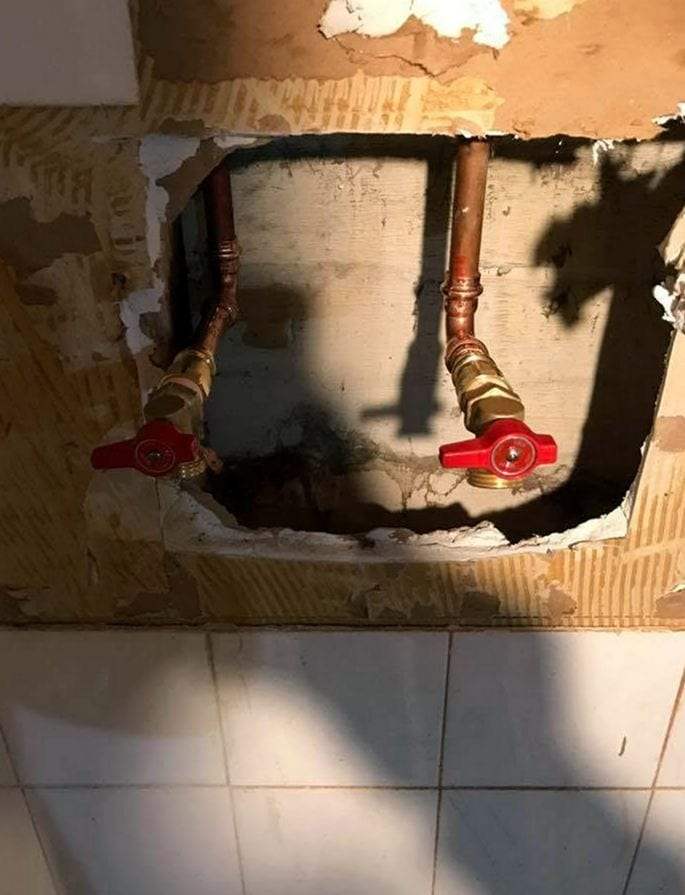 Two new copper supply stub-outs with red-handled ball valves in an opened wall above white tile