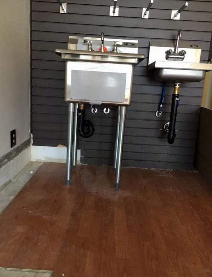 Stainless utility sink and hand sink with chrome faucets and drain lines installed against a slat wall in a commercial space
