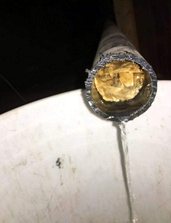 Cut section of drain pipe packed with yellow grease buildup, water trickling past it