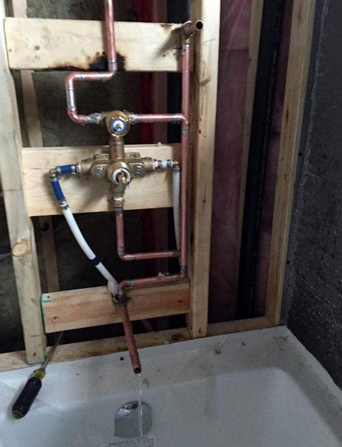 Shower valve rough-in with copper and PEX supply lines in an open wall framed with new lumber above a tub