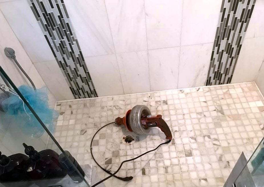Drum drain cleaning machine with its cable fed into the drain of a tiled shower floor