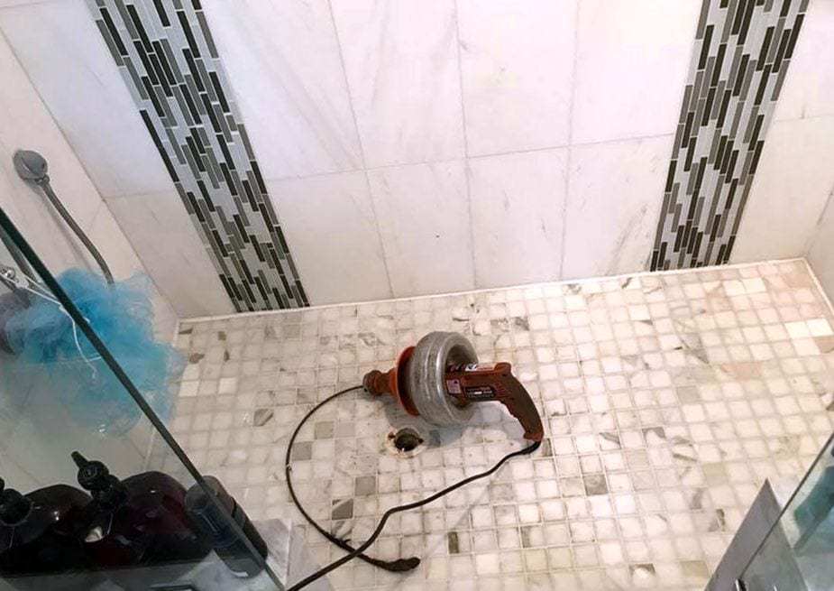 Drum drain cleaning machine with its cable fed into the drain of a tiled shower floor