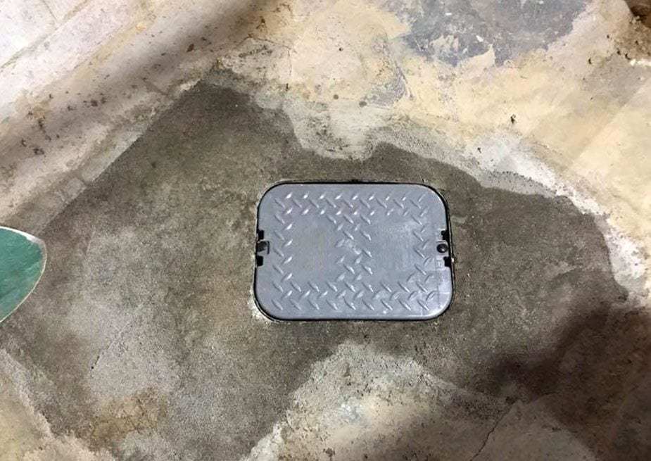 Diamond-plate access cover set in a freshly patched concrete basement floor