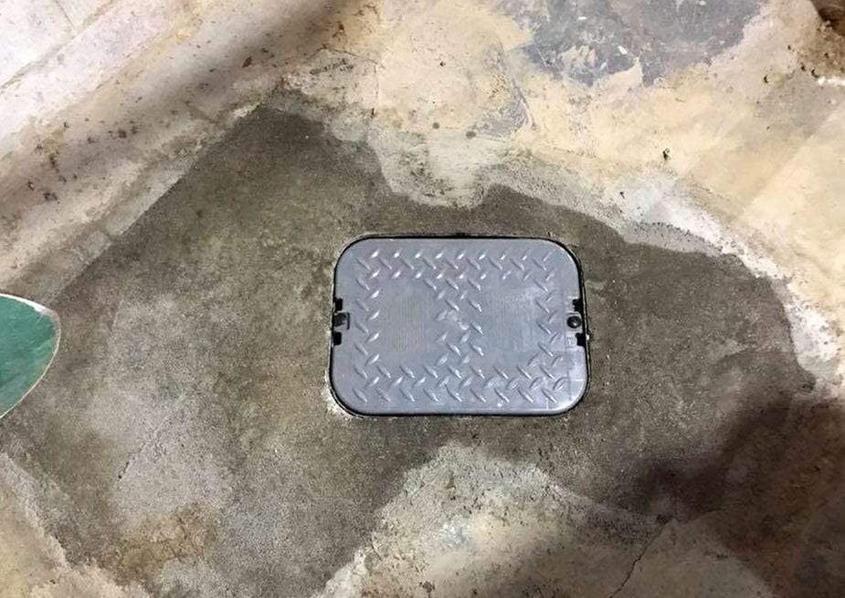 Diamond-plate access cover set in a freshly patched concrete basement floor