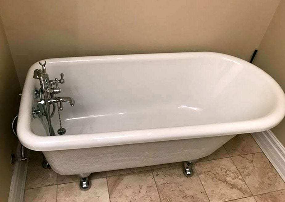 White clawfoot bathtub with a chrome freestanding faucet in a beige bathroom with a tile floor