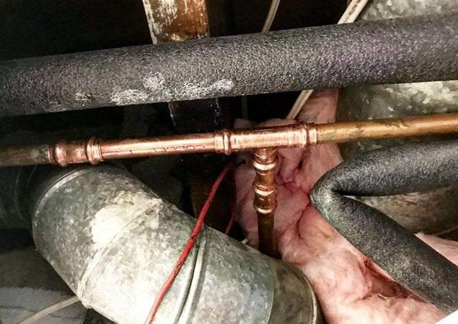 Copper water line with a new tee running between foam-insulated pipes under a floor