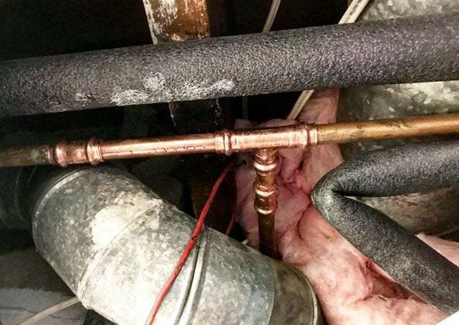 Copper water line with a new tee running between foam-insulated pipes under a floor