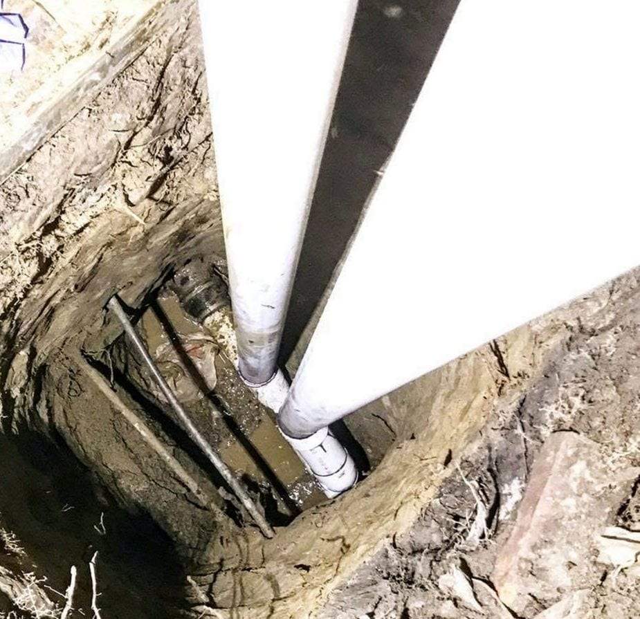 White PVC drain pipes running down into an excavated trench beside a foundation wall