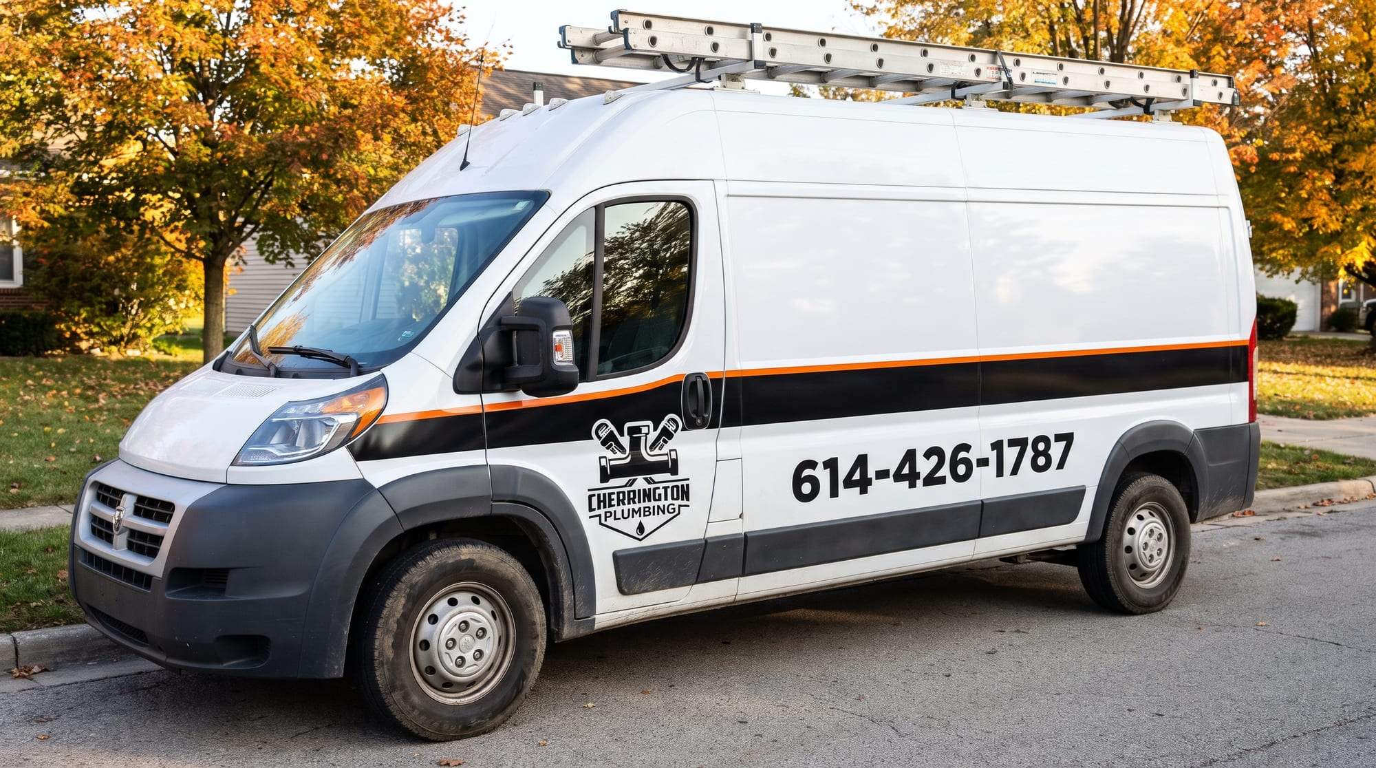 White Cherrington Plumbing van with a black side band, an orange stripe and a ladder rack, parked at the curb on a residential street in autumn